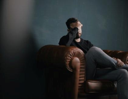 a man sitting on couch with hands on forehead